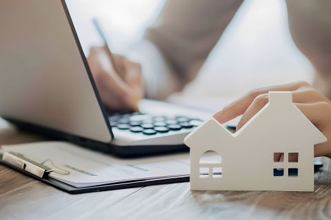 Foto: Person bearbeitet Akten, Modell eines Hauses im Vordergrund